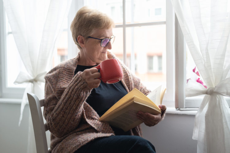 Senior woman enjoying a book at home next to the window.