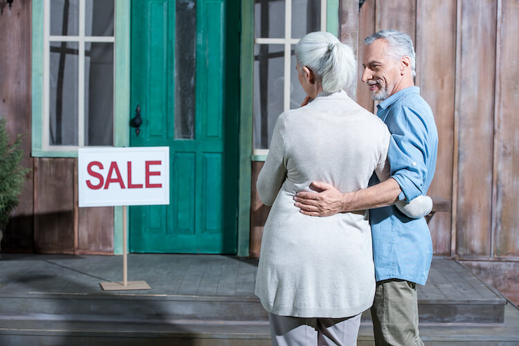 Senior couple admiring the sale sign on their home.