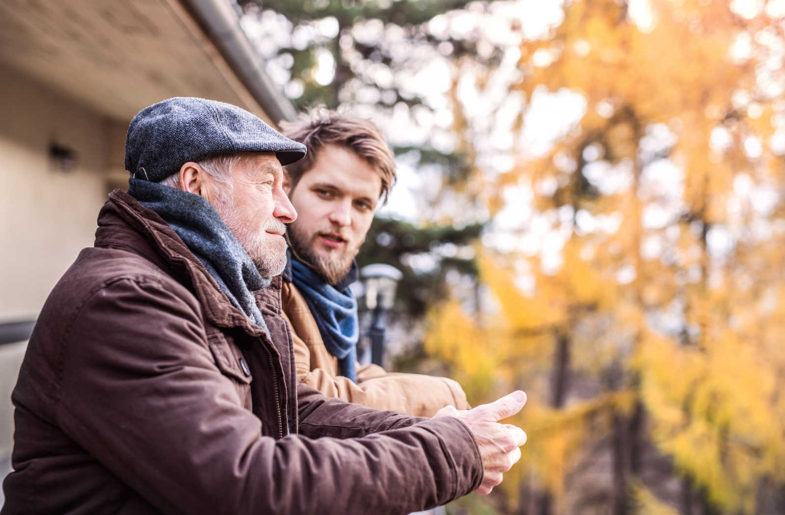 Young man outside in the fall leaning on a railing and speaking to a senior man who is doing the same