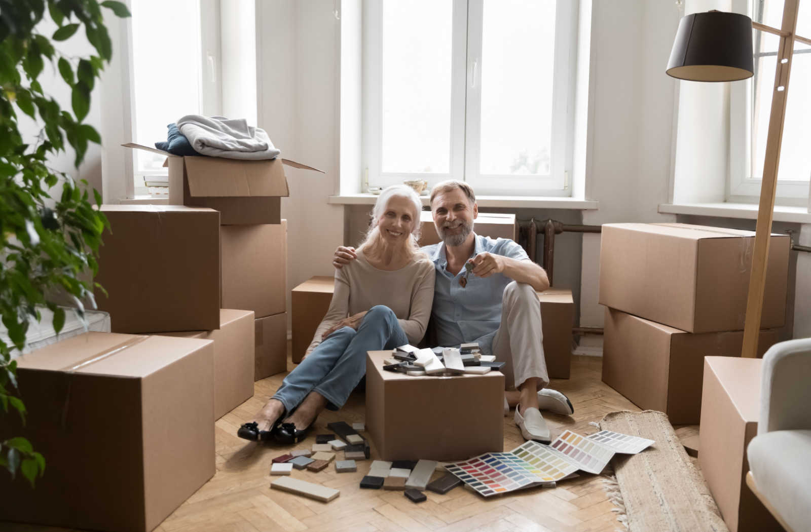 Senior couple sitting on the floor, surrounded by boxes preparing to move into assisted living.